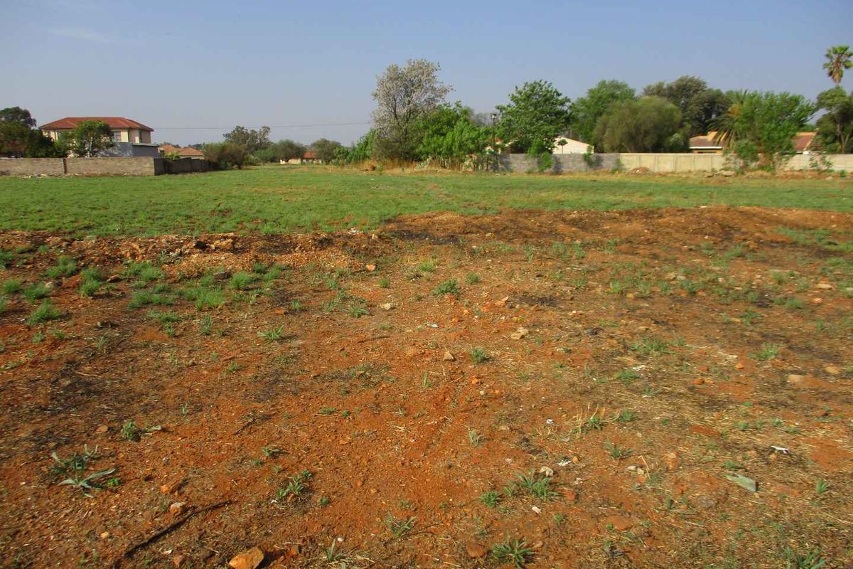A vacant residential plot featuring open grass and soil, enclosed by perimeter boundary walls in a suburban setting.