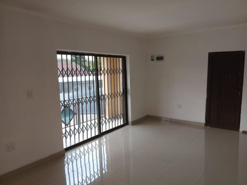 A bright, empty living area featuring neutral tiled flooring, a sliding glass door with a security gate, and clean white walls.