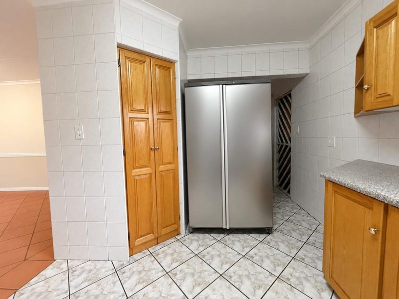 A functional kitchen area featuring tiled walls, built-in wooden cabinetry, and durable tiled flooring, providing a practical workspace with ample storage.