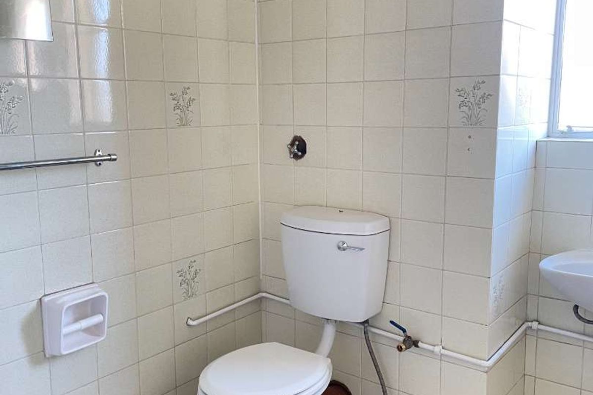 A dated bathroom featuring ceramic wall and floor tiles, a standard toilet, and a washbasin, currently requiring cosmetic updates and maintenance.