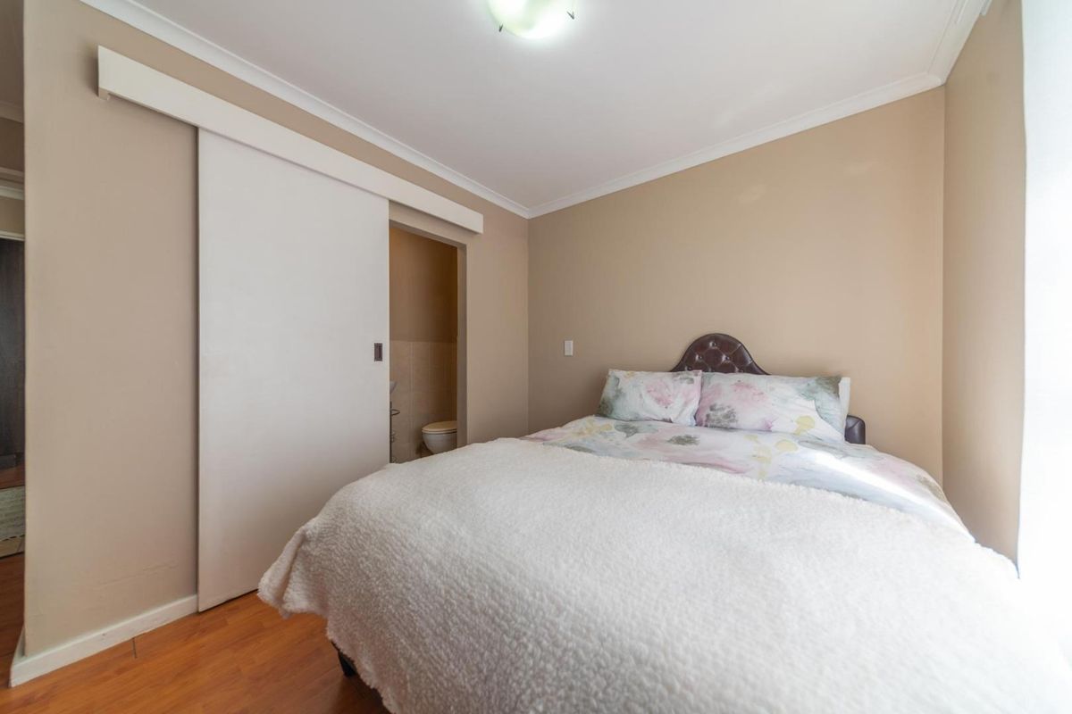 A well-maintained bedroom featuring laminate flooring, coving, and a convenient sliding door providing access to an en-suite bathroom.