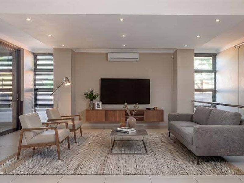 Modern living room featuring recessed lighting, a floating media console, split-system air conditioning, and a sleek staircase with stainless steel and cable railing.