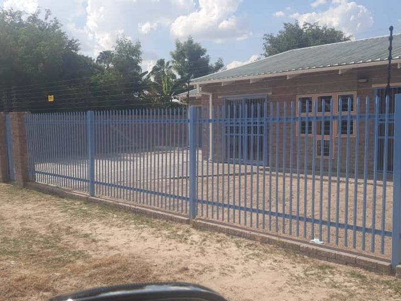 Front exterior view of the property featuring secure steel palisade fencing, electric security wires, and a paved driveway area.