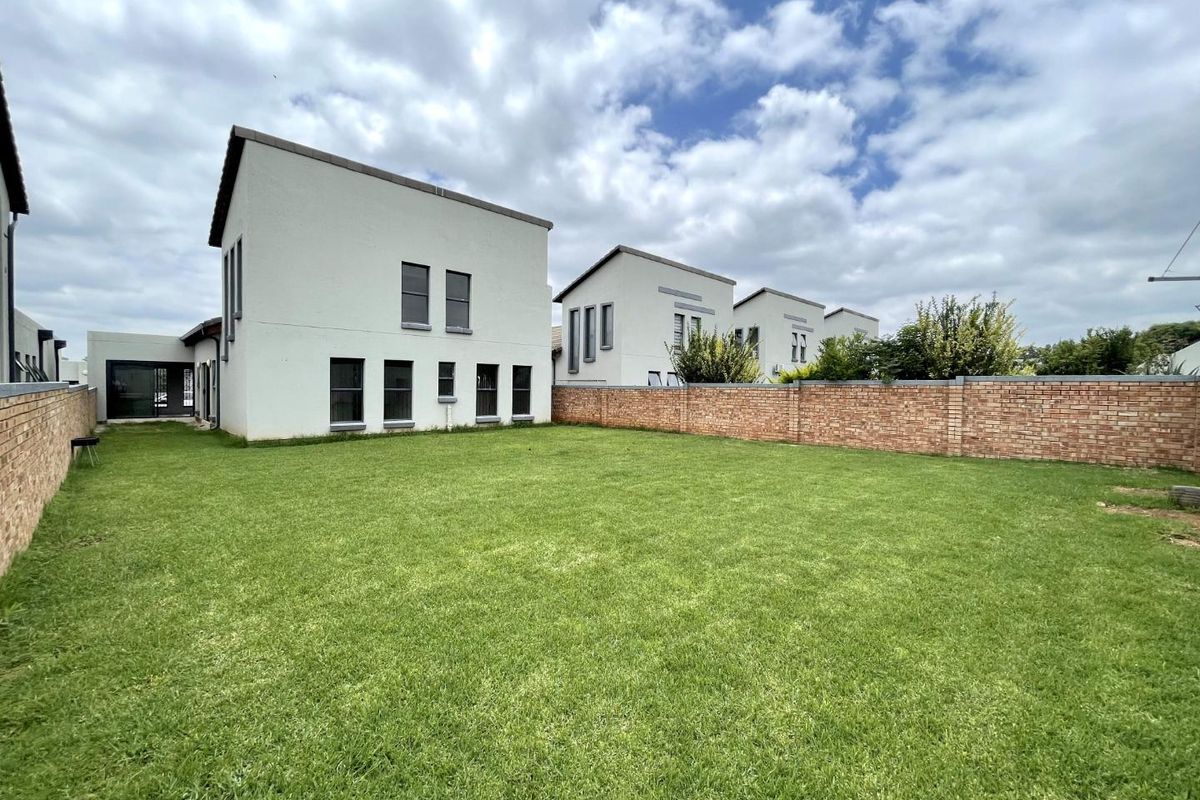 A spacious rear garden featuring a well-maintained lawn and a brick boundary wall, adjacent to the rear facade of the townhouse.