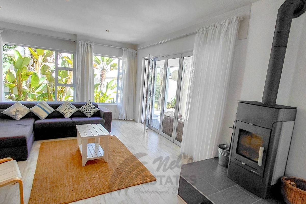 Bright living room featuring large windows, tiled flooring, and a built-in fireplace, with direct access to the outdoor patio area.