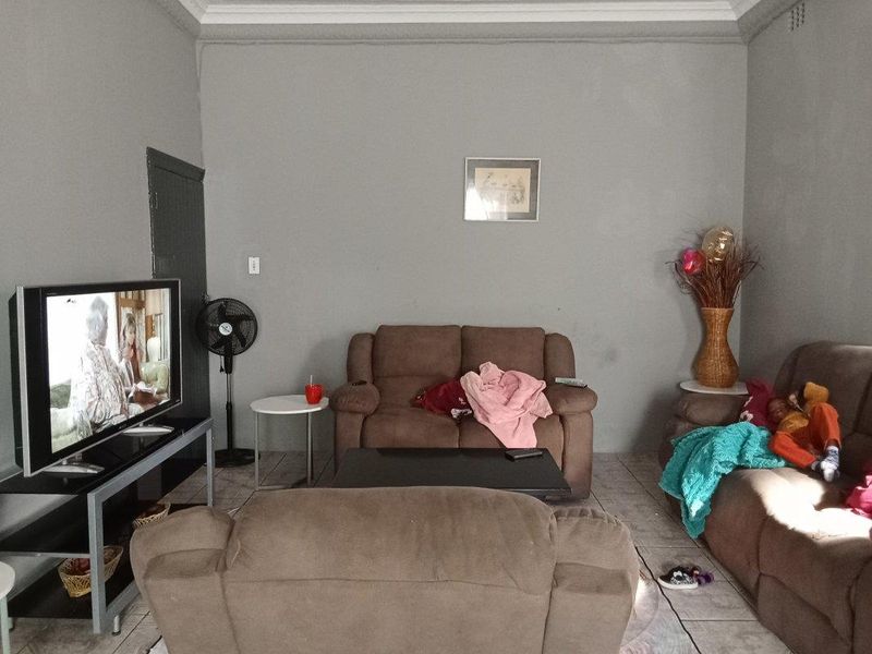 A living room featuring tiled flooring and coving, currently showing signs of wear on the wall surfaces.