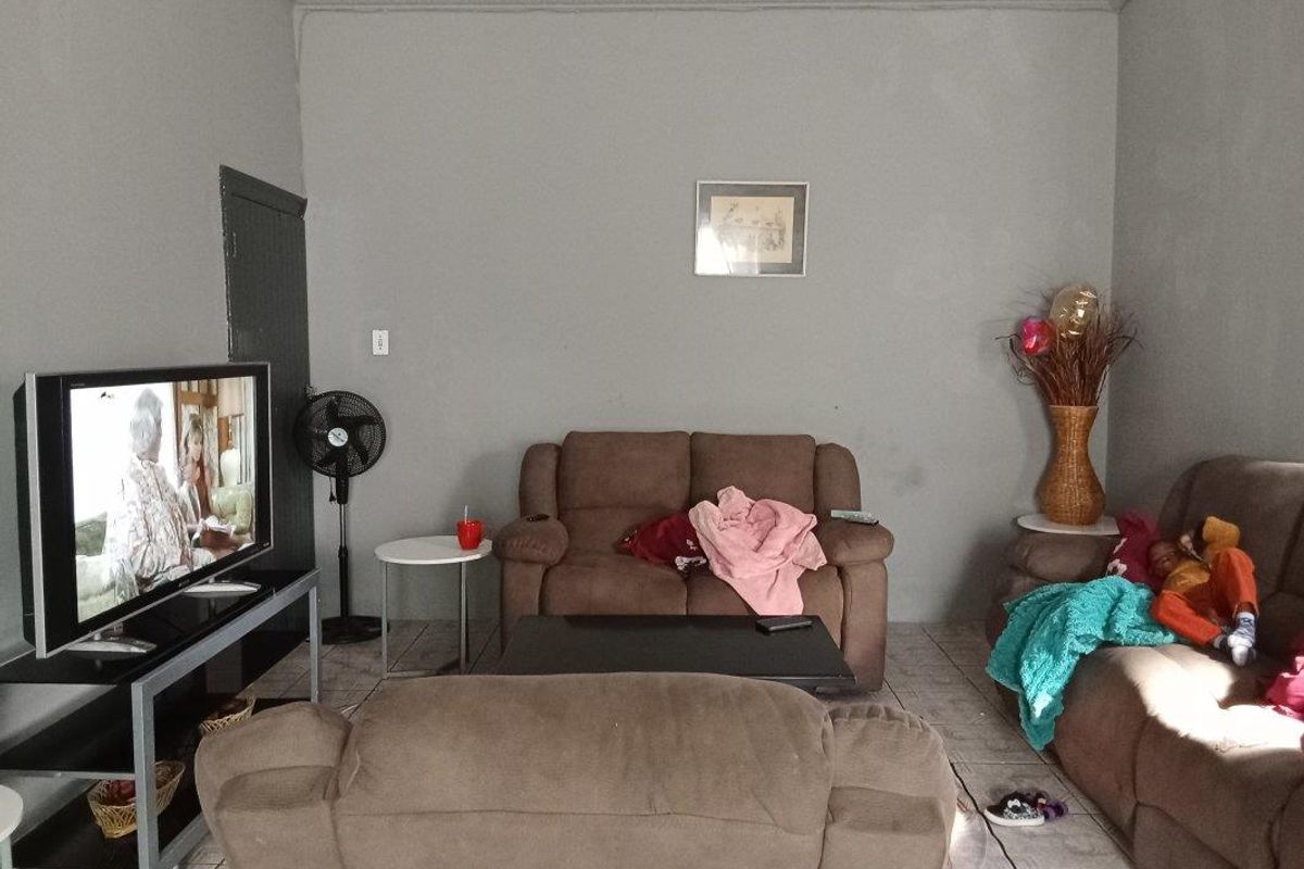 A living room featuring tiled flooring and coving, currently showing signs of wear on the wall surfaces.