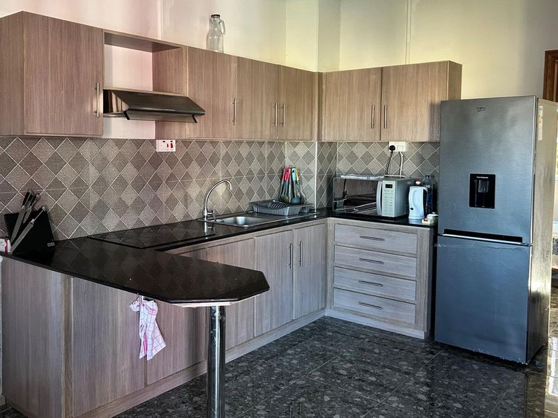 A functional kitchen featuring wood-look laminate cabinetry, granite countertops, a diamond-patterned tile backsplash, and a convenient breakfast bar extension.