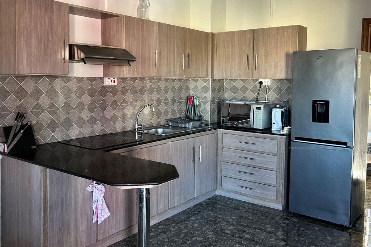 A functional kitchen featuring wood-look laminate cabinetry, granite countertops, a diamond-patterned tile backsplash, and a convenient breakfast bar extension.