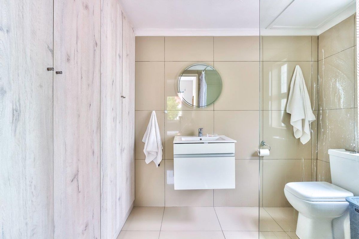 Modern bathroom featuring a wall-mounted vanity, glass shower enclosure, neutral tiled finishes, and ample built-in storage cabinetry.