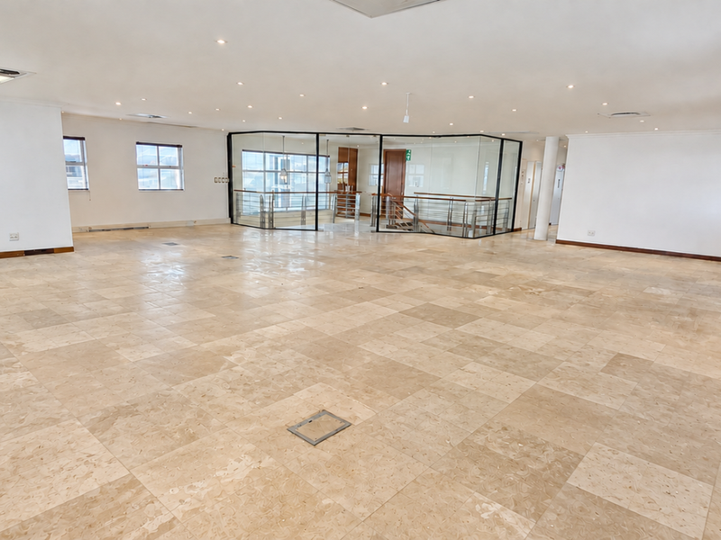 Spacious open-plan office area featuring polished stone tile flooring, recessed lighting, and a modern glass-enclosed partition.