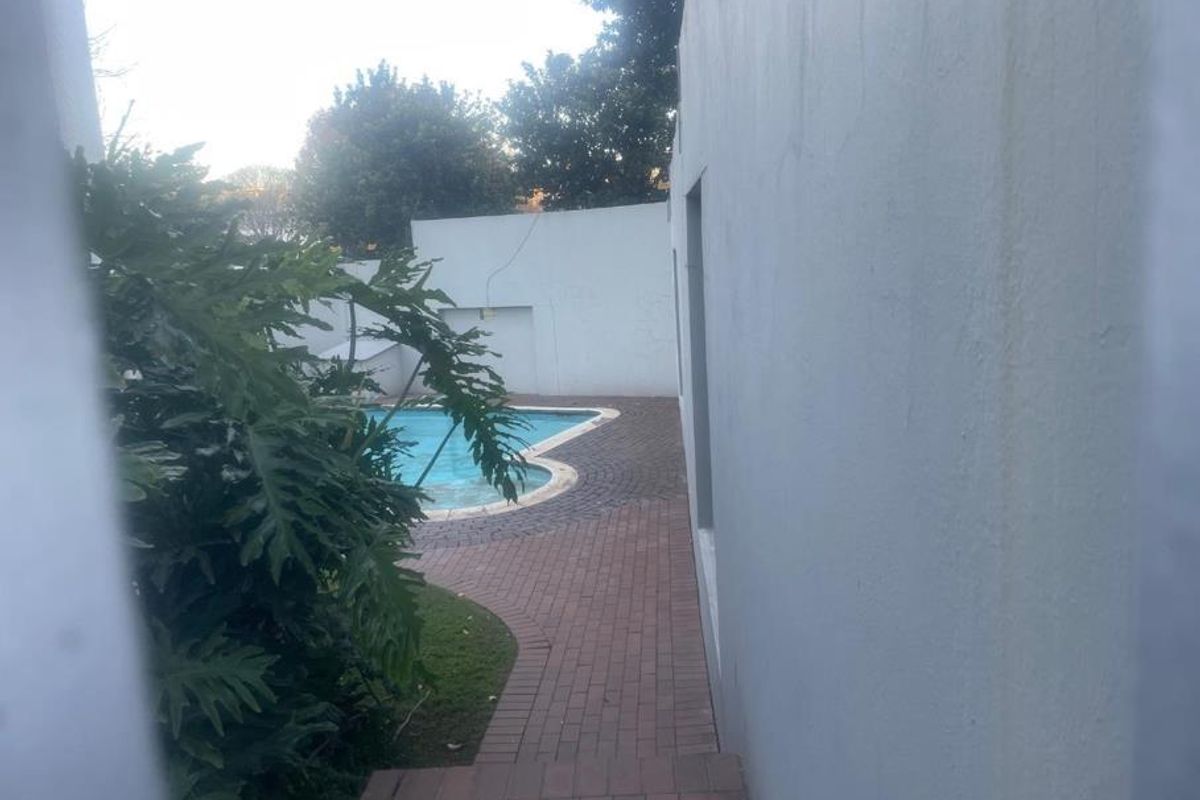 Outdoor pool area featuring a swimming pool, brick paved walkway, and surrounding boundary walls.