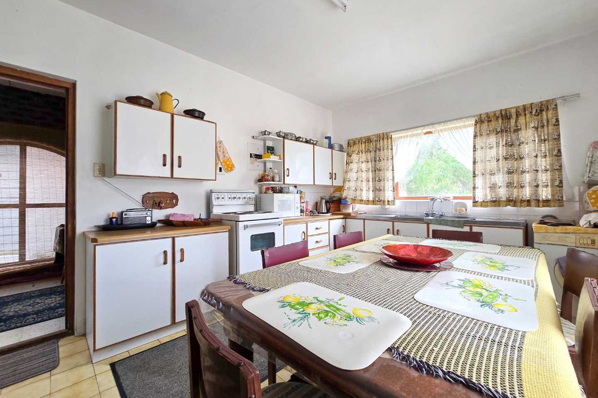 A dated kitchen featuring original cabinetry, a freestanding stove, and a dining area, offering significant potential for modernization and renovation.