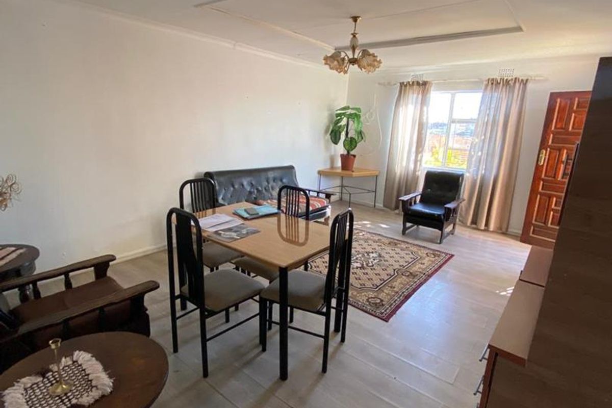 A spacious living and dining area featuring light-toned laminate flooring, a central ceiling light fixture, and a solid timber entrance door.