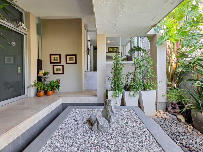 A well-maintained covered patio area featuring tiled flooring, a decorative stone garden bed, and direct access to the interior through sliding glass doors.