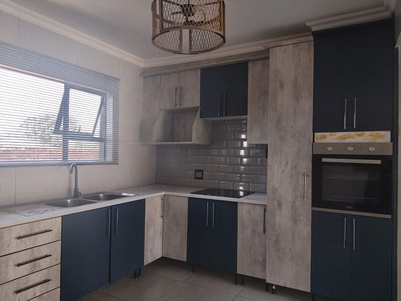 Modern kitchen featuring two-tone cabinetry, subway tile backsplash, built-in oven, electric hob, and double sink with contemporary fixtures.