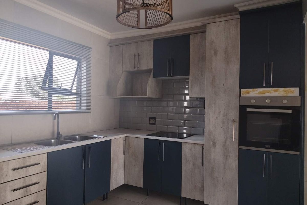 Modern kitchen featuring two-tone cabinetry, subway tile backsplash, built-in oven, electric hob, and double sink with contemporary fixtures.
