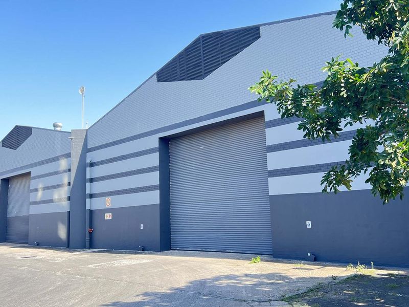 Exterior view of a modern industrial warehouse facility featuring large roller shutter doors, brick facade, and high-level ventilation louvres.