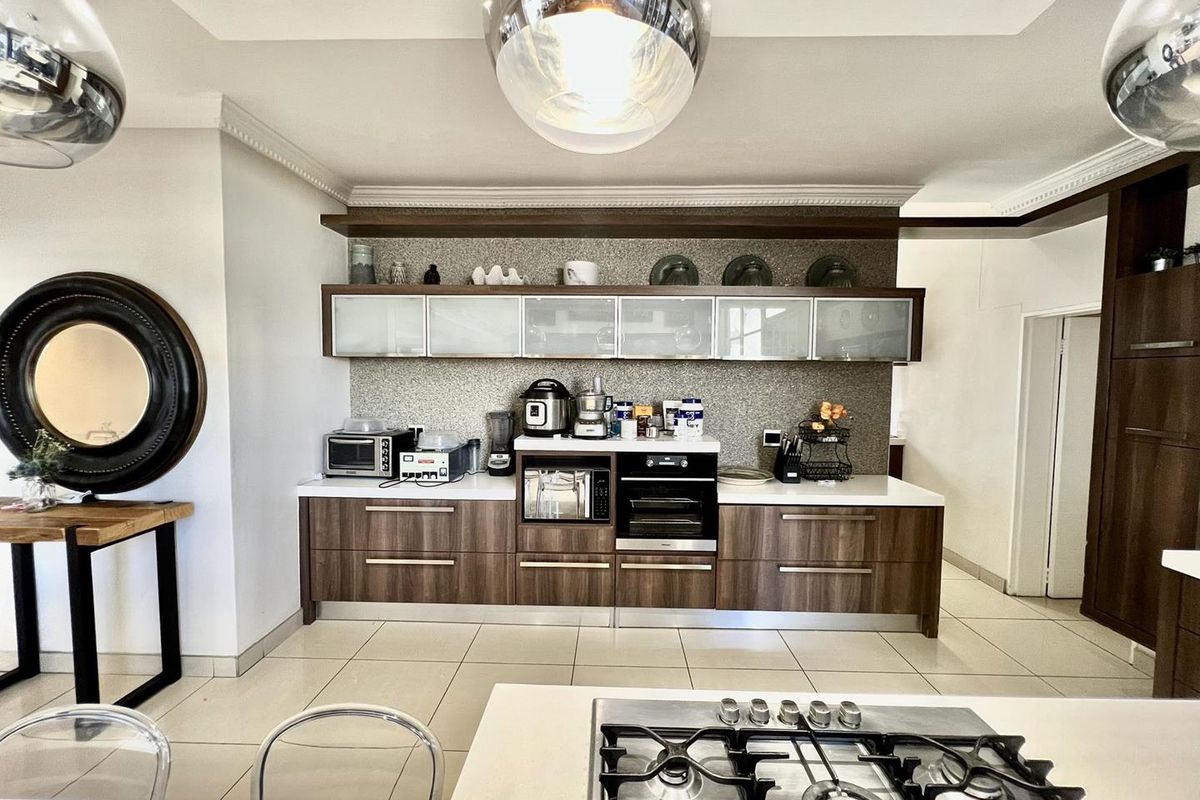 Modern kitchen featuring dark wood cabinetry, white stone countertops, integrated oven, and a gas hob on the central island.