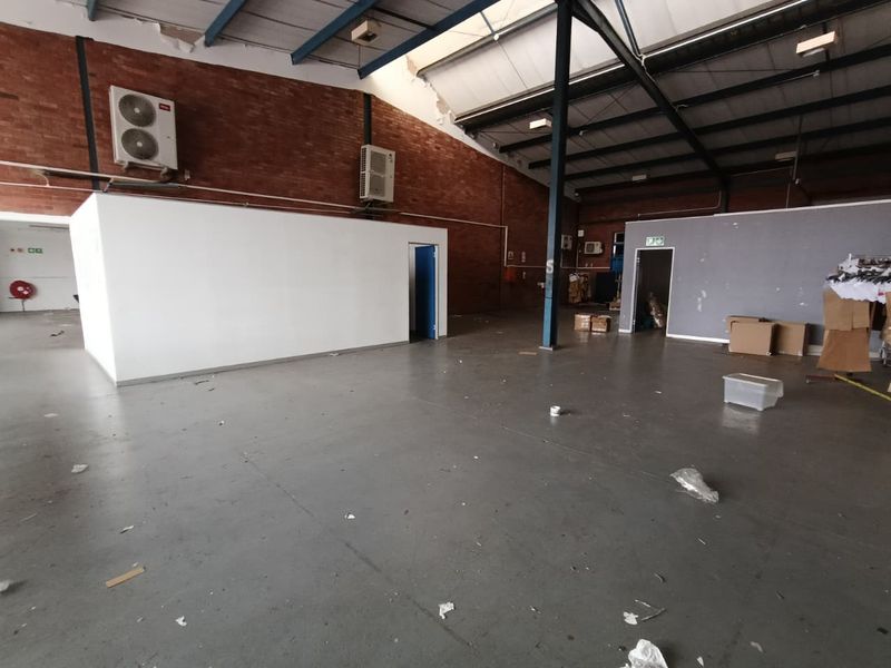 Spacious industrial utility area featuring exposed brick walls, steel roof trusses, concrete flooring, and wall-mounted air conditioning units.