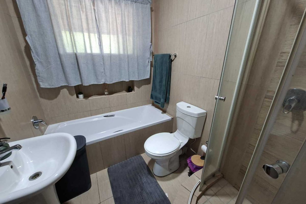 A functional bathroom featuring a bathtub, separate shower enclosure, pedestal basin, and toilet with neutral wall and floor tiling.
