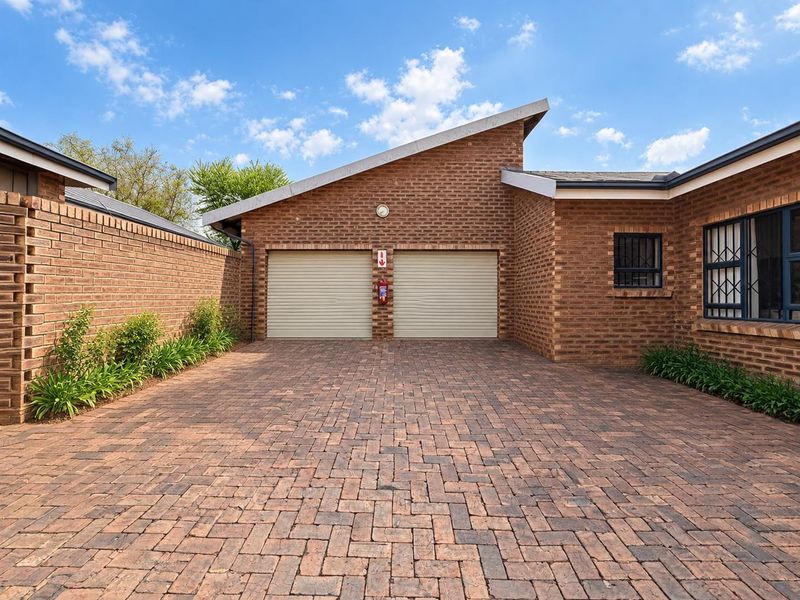 A well-maintained double garage with a brick facade and a neat paved driveway, featuring secure window bars and exterior lighting.