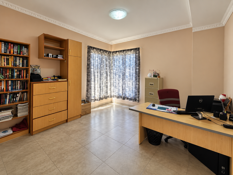 A functional home office featuring tiled flooring, crown molding, and ample natural light through corner windows.