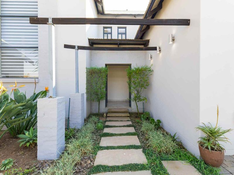 A welcoming entrance featuring a stone paver walkway, timber pergola structure, and landscaped garden beds leading to the main doorway.