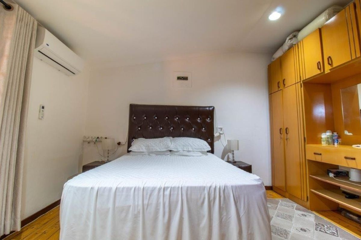 A functional bedroom featuring timber flooring, a built-in wardrobe with integrated vanity, and a wall-mounted split-system air conditioner.