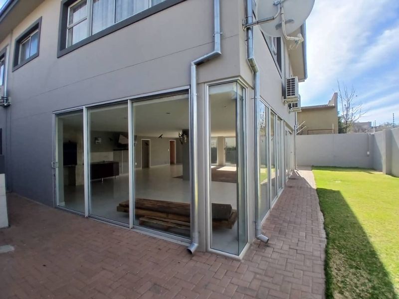 Rear view of the property featuring extensive sliding glass doors, a paved patio area, and a well-maintained garden with boundary walls.