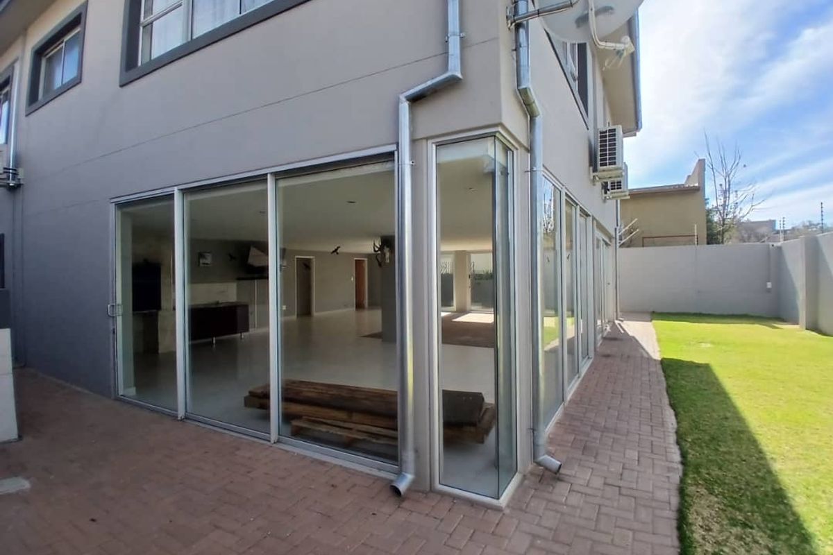 Rear view of the property featuring extensive sliding glass doors, a paved patio area, and a well-maintained garden with boundary walls.