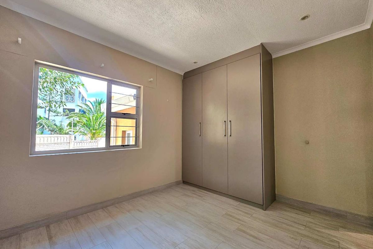 A bright, empty bedroom featuring neutral wall tones, modern tiled flooring, and a large built-in wardrobe with ample storage space.