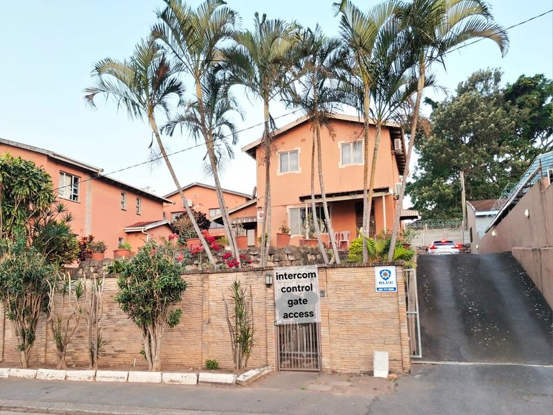 Front elevation of a multi-story residential property featuring a brick boundary wall, secure gated entrance, and an asphalt driveway.