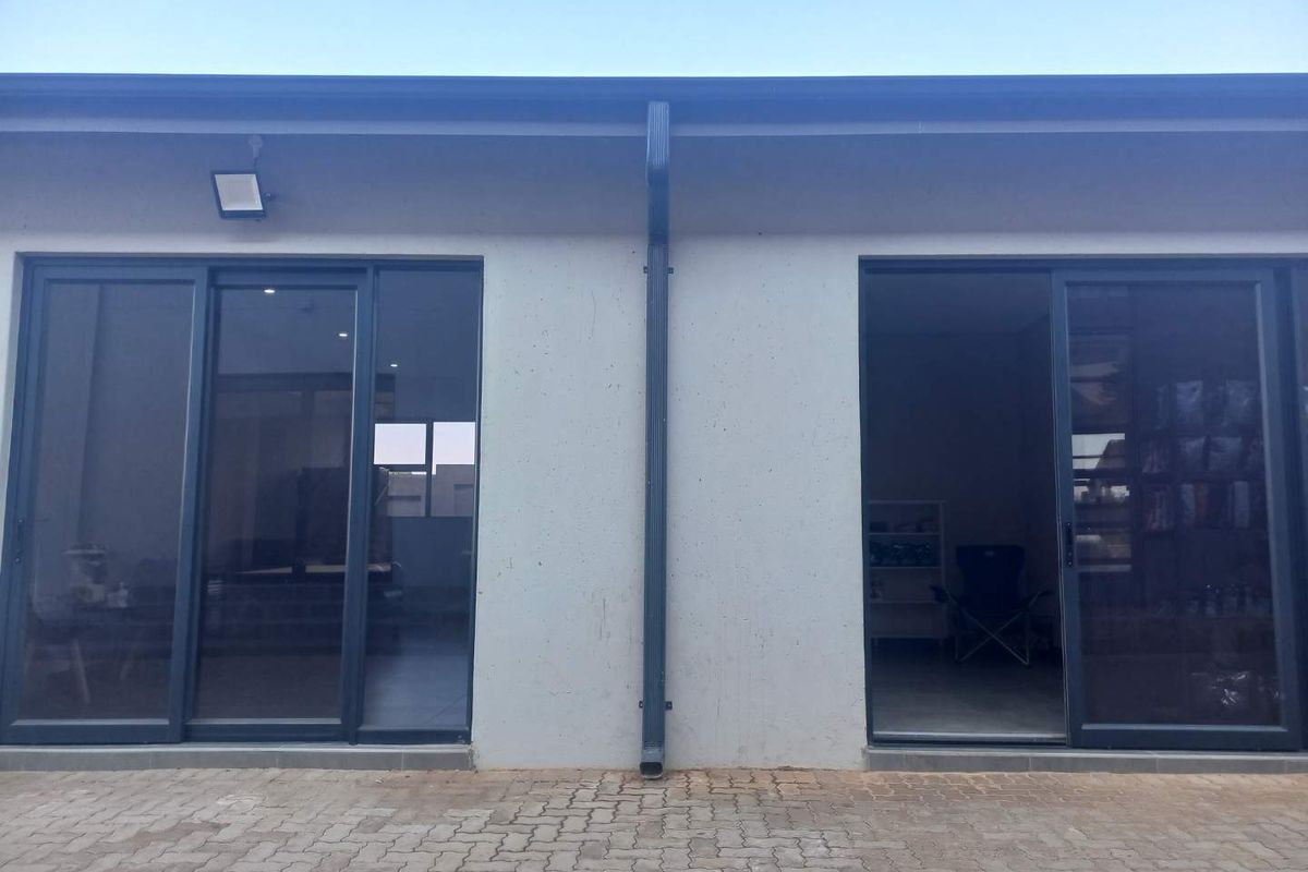 Rear exterior view of the property featuring dual sliding glass doors, a paved patio area, and a central downpipe.