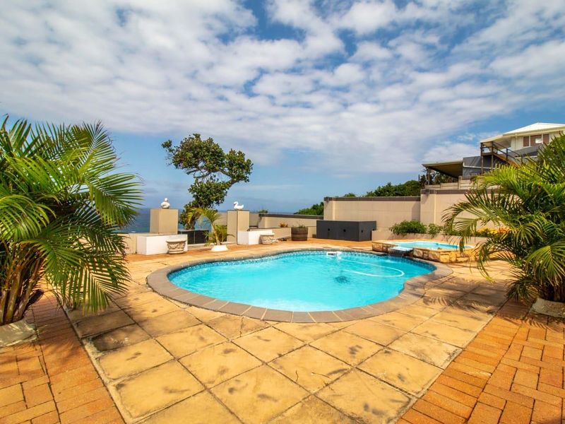 Outdoor pool area featuring a swimming pool with a water feature, surrounded by paved patio space and retaining walls with ocean views.