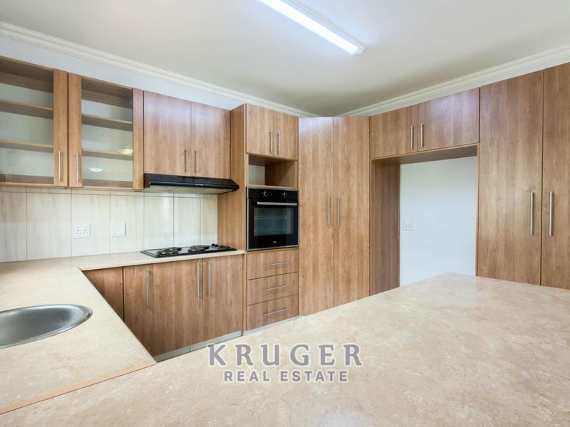 A clean, modern kitchen featuring wood-finish cabinetry, stone-look countertops, built-in oven, gas hob, and ample storage space.