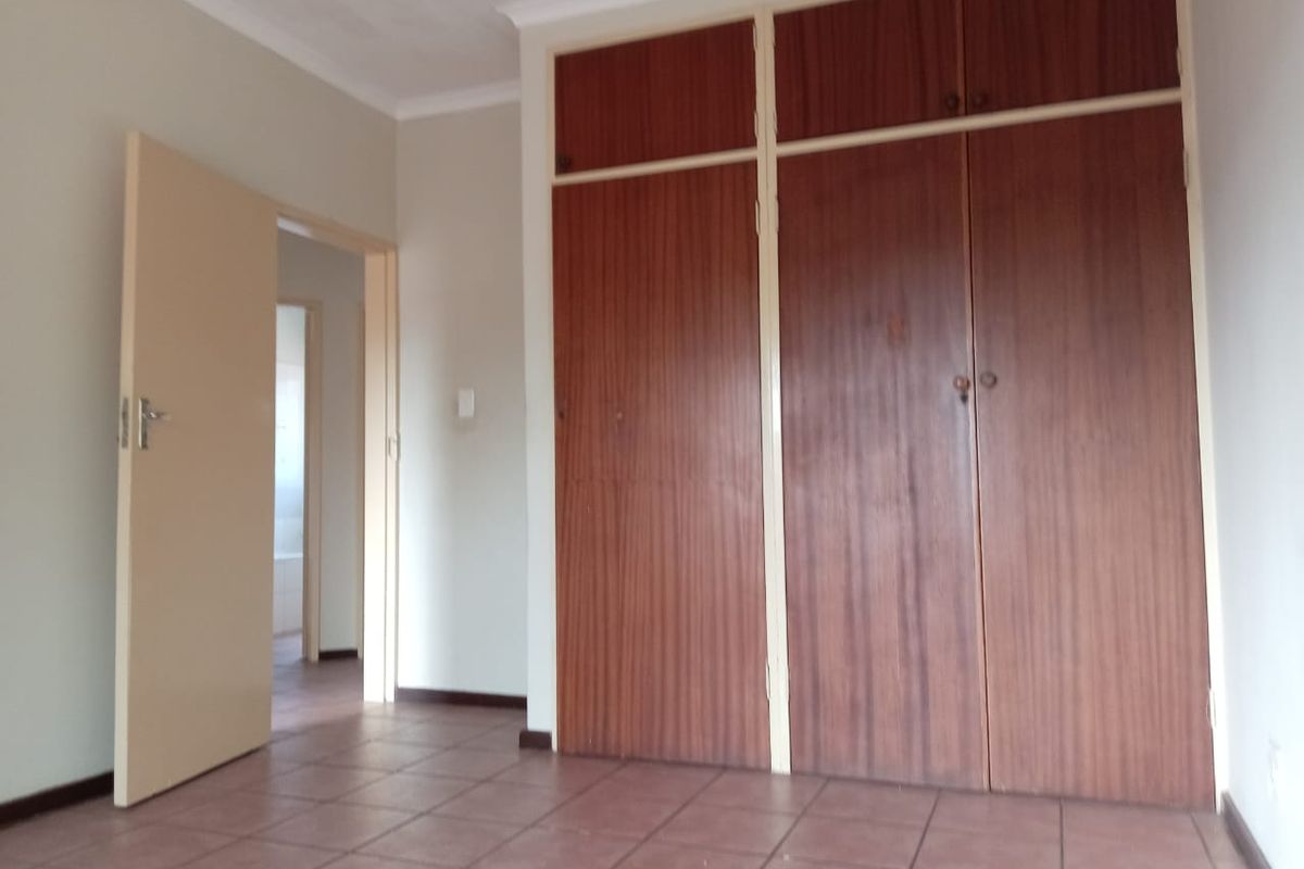 An empty bedroom featuring tiled flooring and a large built-in wooden wardrobe with overhead storage compartments.