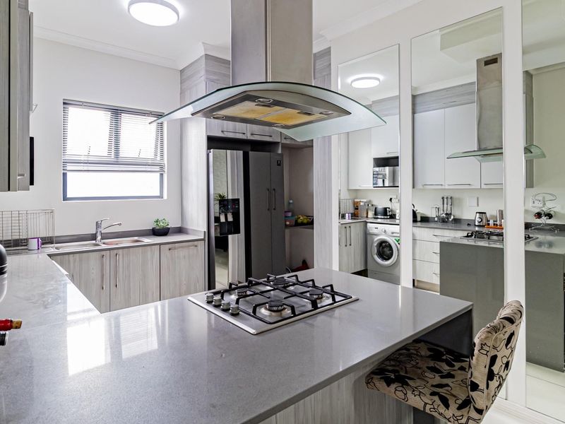 Modern kitchen featuring stone countertops, a central gas hob with extractor, ample built-in cabinetry, and a separate laundry area with integrated appliances.