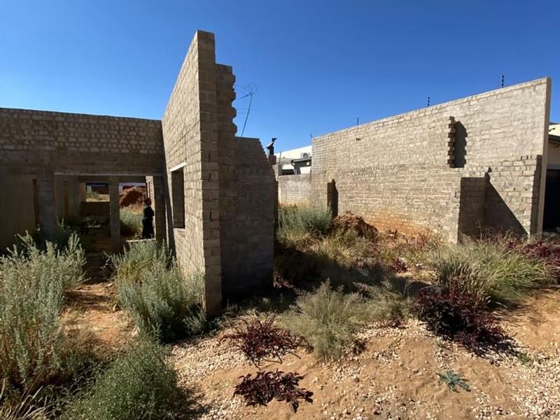 An unfinished residential construction site showing exposed brick walls and structural masonry in a shell state, requiring significant completion work.