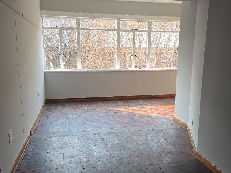 An empty living area featuring original parquet flooring and large windows that provide ample natural light.