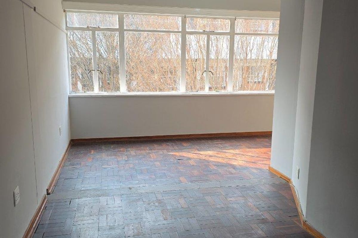An empty living area featuring original parquet flooring and large windows that provide ample natural light.