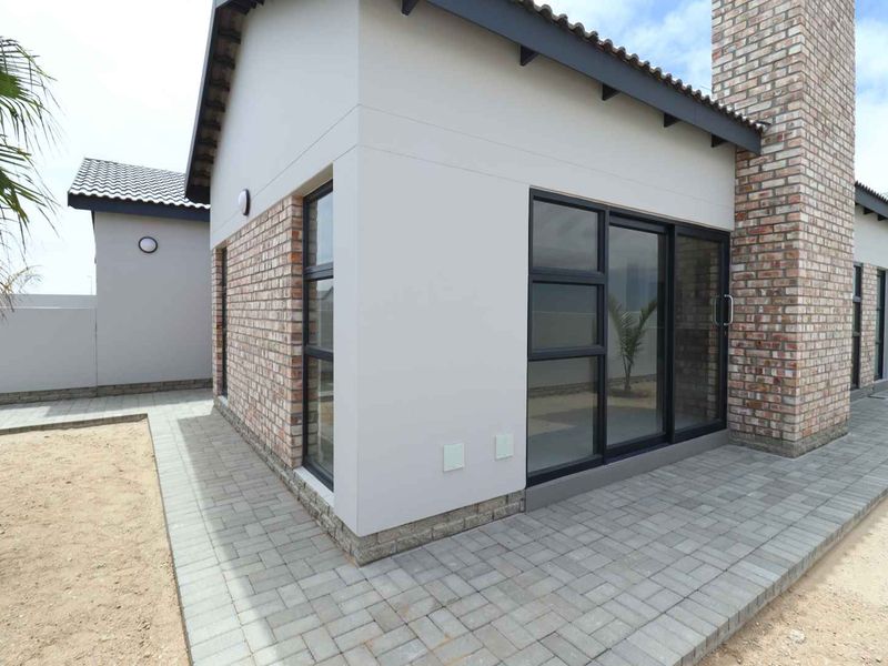 Rear view of a modern house featuring a paved patio, brick chimney, and large sliding glass doors with dark frames.