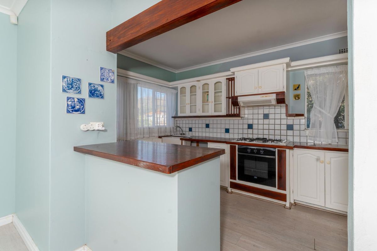 A functional kitchen featuring white cabinetry, a built-in oven and gas hob, tiled backsplash, and a wooden breakfast bar counter.