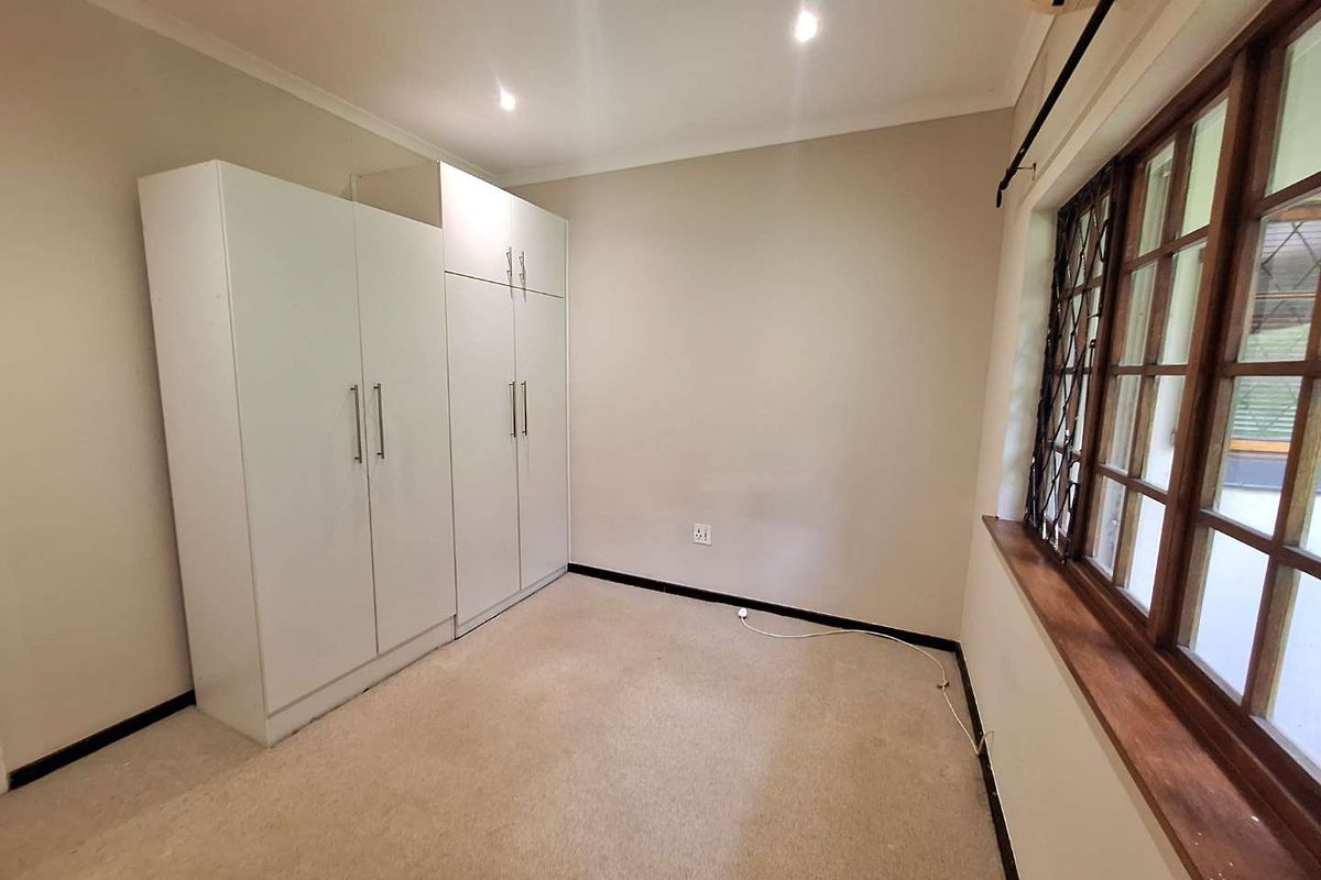 A vacant bedroom featuring built-in cupboards, wooden window frames with security bars, and an air conditioning unit.