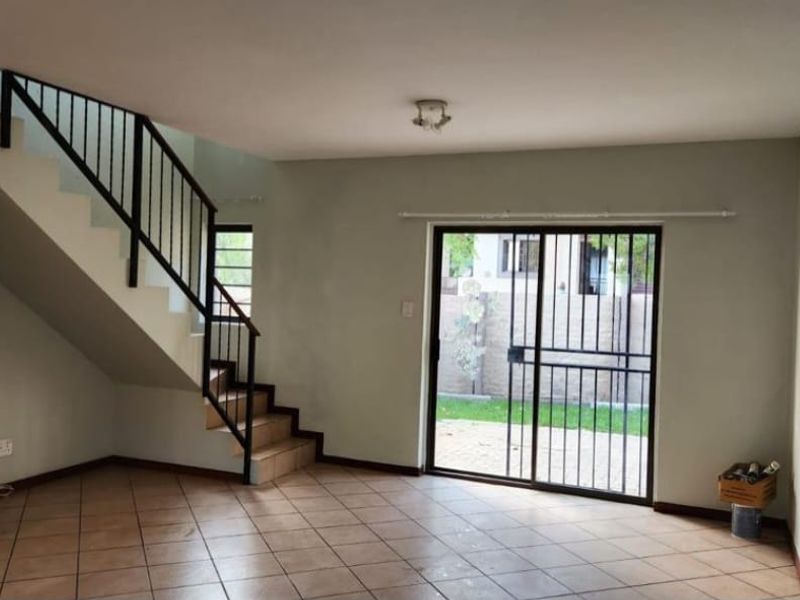 An open-plan living area featuring tiled flooring, a staircase with a metal balustrade, and a sliding glass door leading to the exterior.