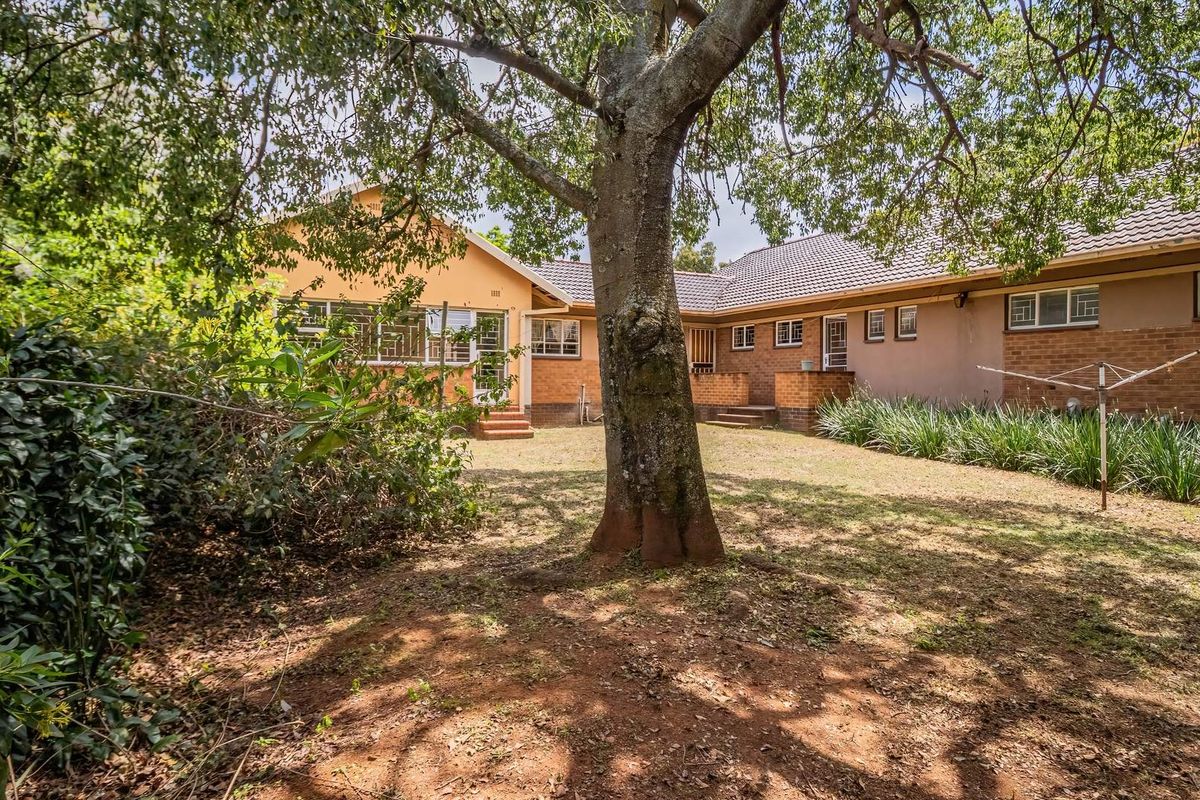A spacious rear garden featuring a large mature tree, established landscaping, and a brick-faced house with a tiled roof and security-barred windows.