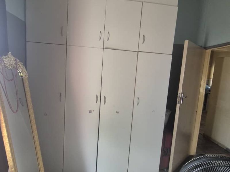 Bedroom featuring built-in cupboards and tiled flooring, showing signs of wear and ceiling water damage.