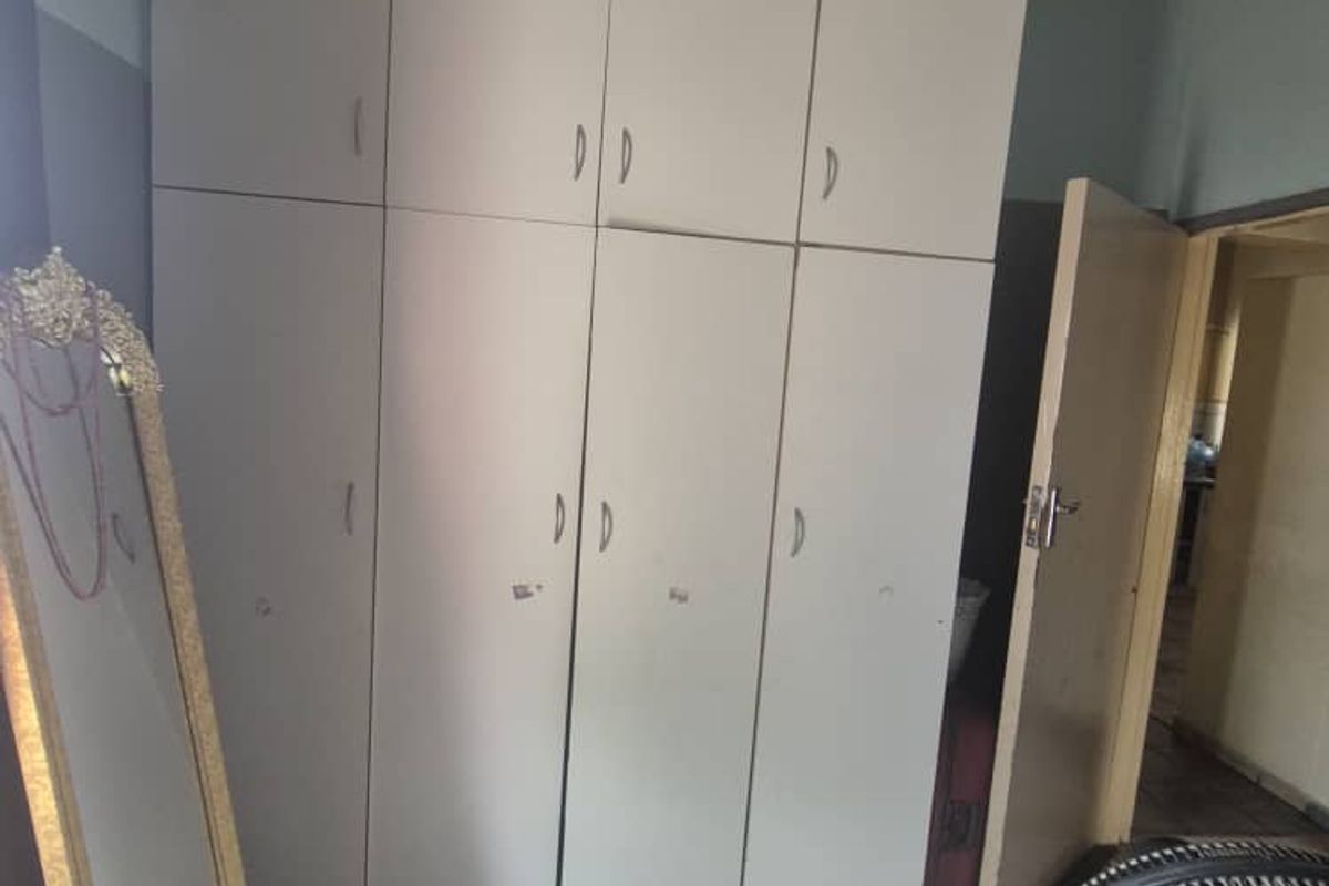 Bedroom featuring built-in cupboards and tiled flooring, showing signs of wear and ceiling water damage.