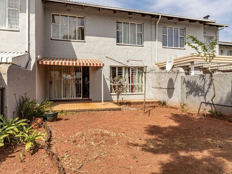 Rear view of the townhouse featuring a paved patio with a striped awning, metal-framed windows, and a private garden space.