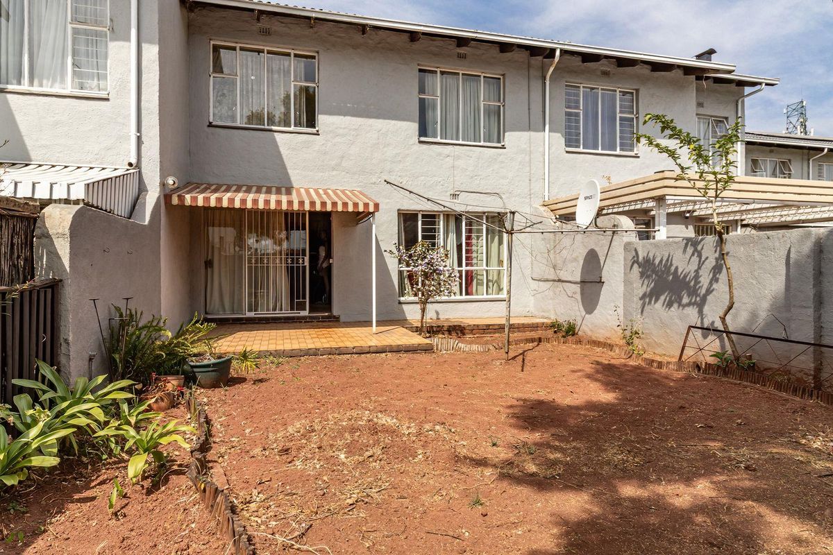 Rear view of the townhouse featuring a paved patio with a striped awning, metal-framed windows, and a private garden space.